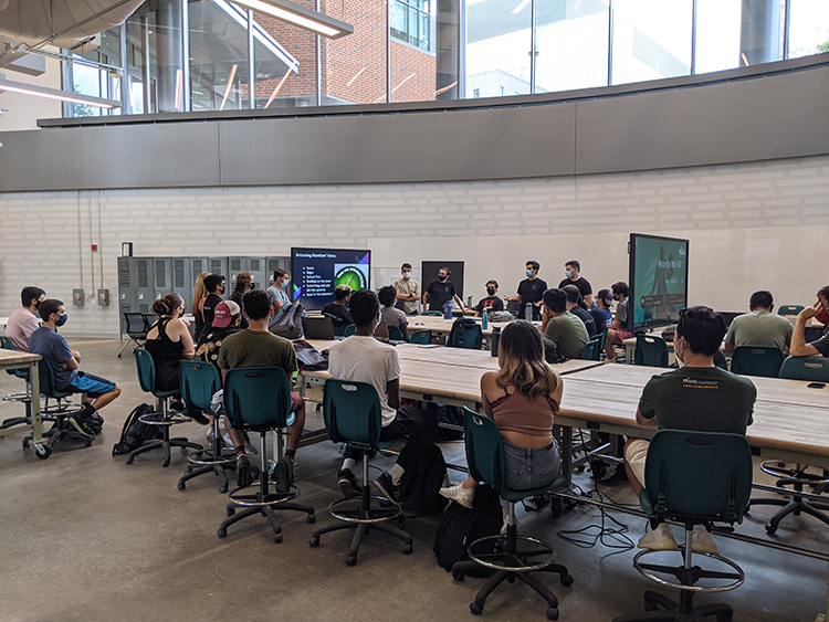 Students at a workshop sit around a table looking at a powerpoint