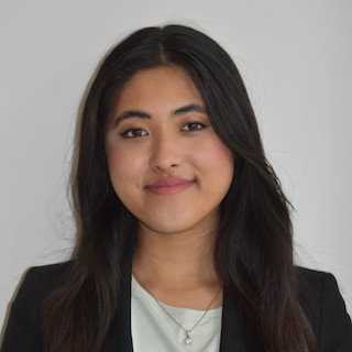 Law student Sahara Shrestha smiles at the camera. She is wearing a black blazer and a white shirt.