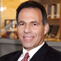 A smiling man in a gold sport coat looks at the camera.