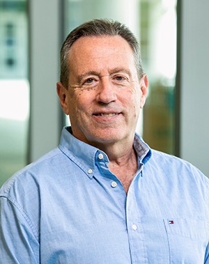 A man in a dress shirt smiles at the camera.