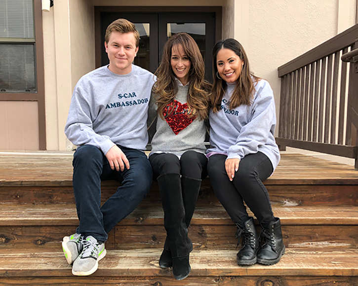 John Casey, Leslie Durham and Gracie Billingsley sitting on steps in front of an S-CAR trailer and smiling for the camera.