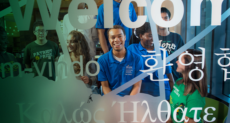 A group of international Mason students smile behind a decorated window in the Ángel Cabrera Global Center. 