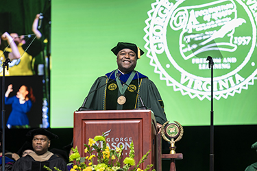University President Gregory Washington stands at the podium, looking out towards the not visible crowd of graduates.