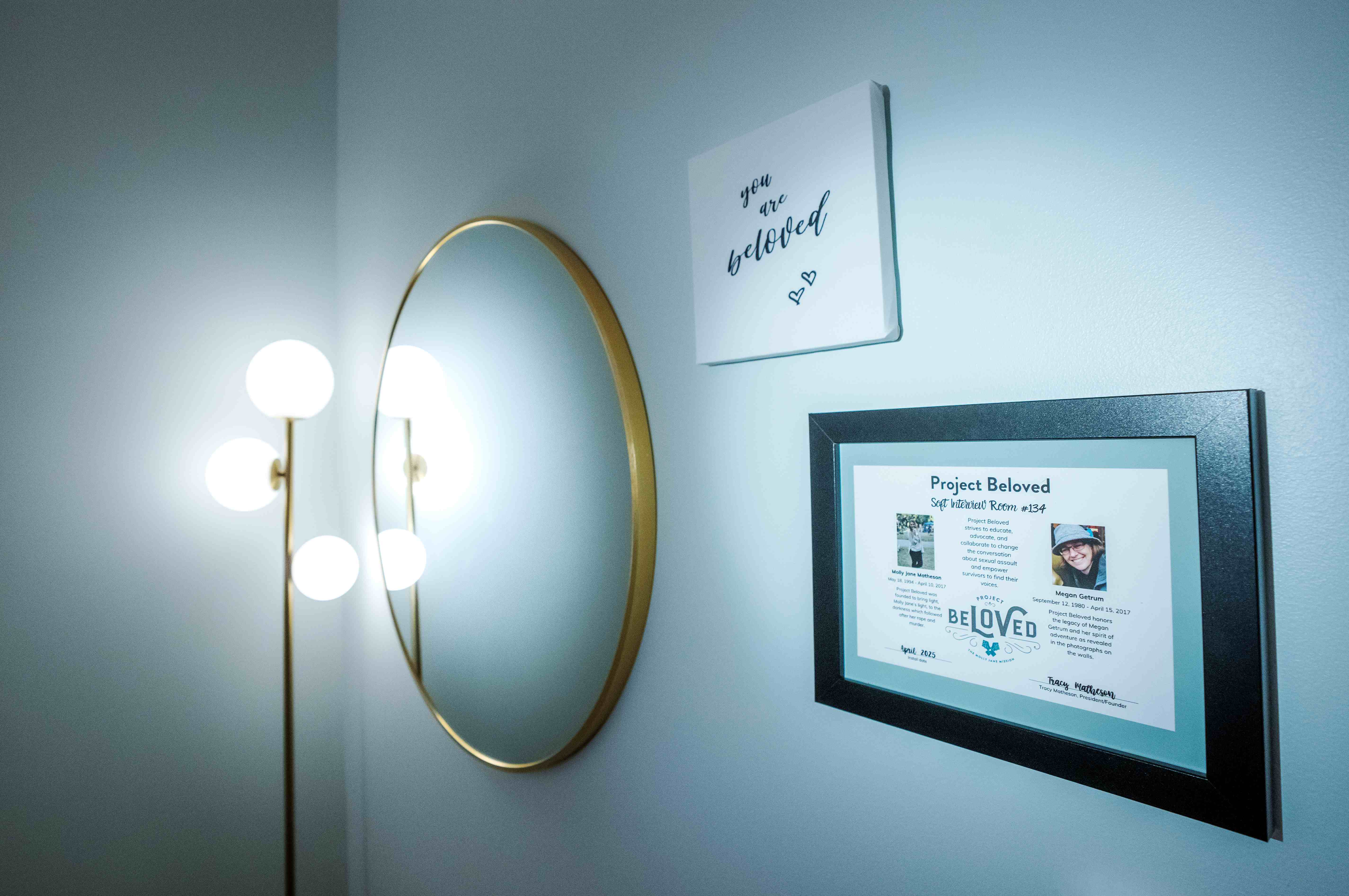 A wall in the soft interview room has a mirror with a canvas hung nearby that says "You are beloved"