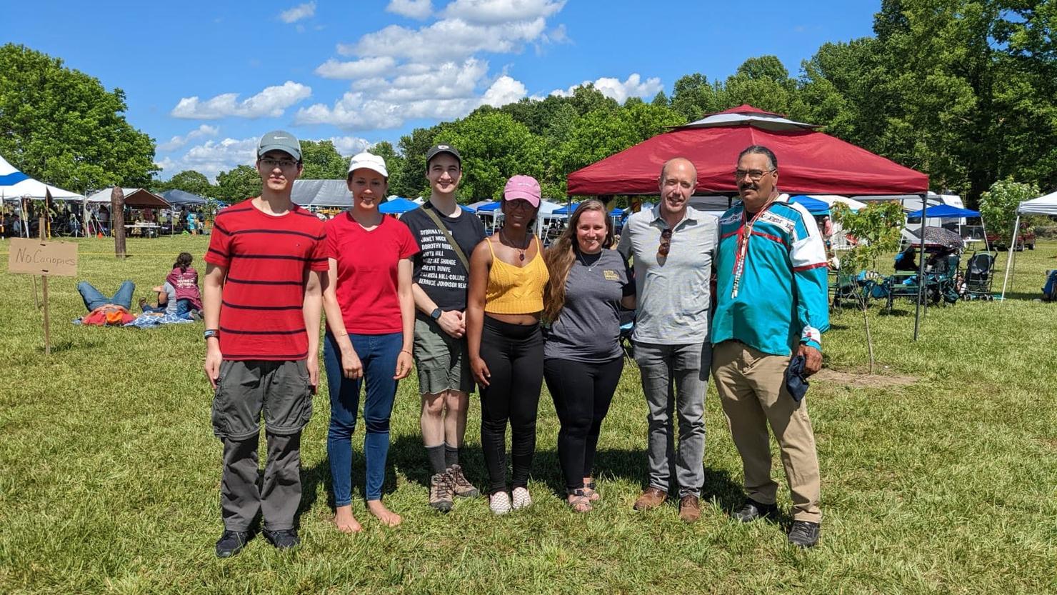 The Mason team and Upper Mattaponi Chief Frank Adams stand shoulder to shoulder for a photo outdoors on a sunny day.