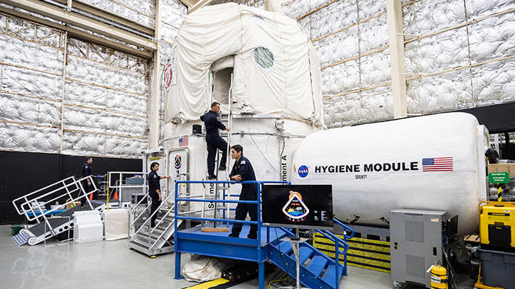 The Human Exploration Research Analog habitat with four astronauts moving around outside it.