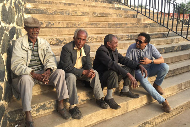 S-CAR Ph.D. student Felegebirhan Mihret sitting on steps and chatting with a group of local men in Asmara.