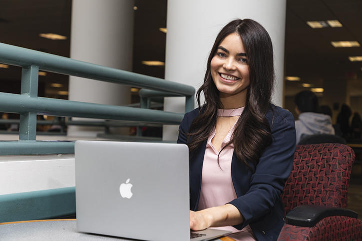 Jennifer Kasse-Wanzer sitting and working on her laptop. She is smiling at the camera.