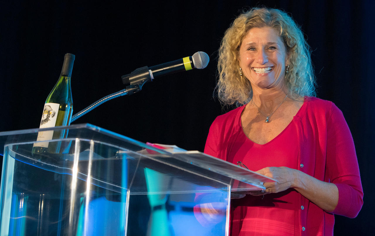 Terri Beirne speaking at a podium. A bottle of Geo. Mason Wine is on the podium.