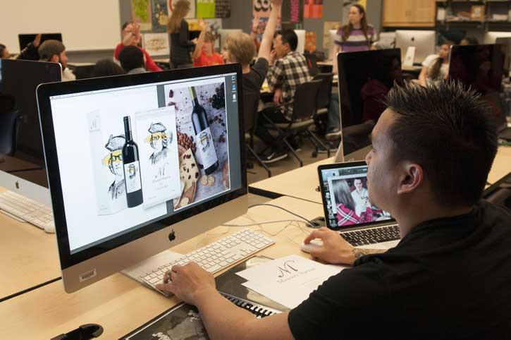 A student working on a computer. The monitor shows that he is working on designs for the new Geo. Mason Wine label.