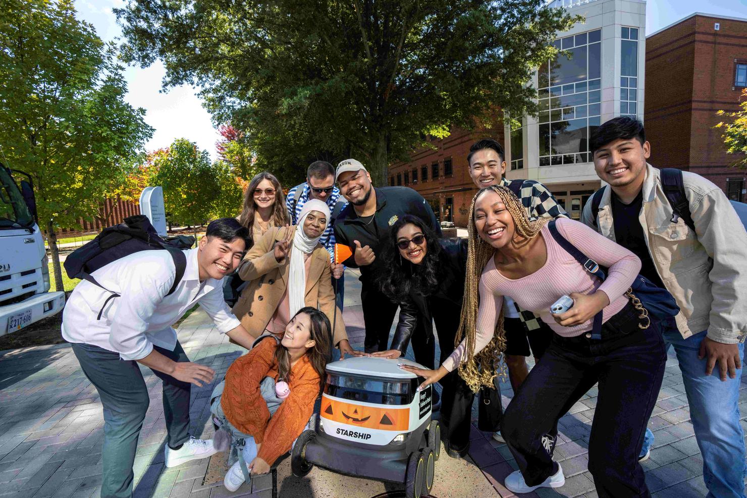 Students group up for a selfie with a Starship Robot that has been decorated with a Halloween decal.