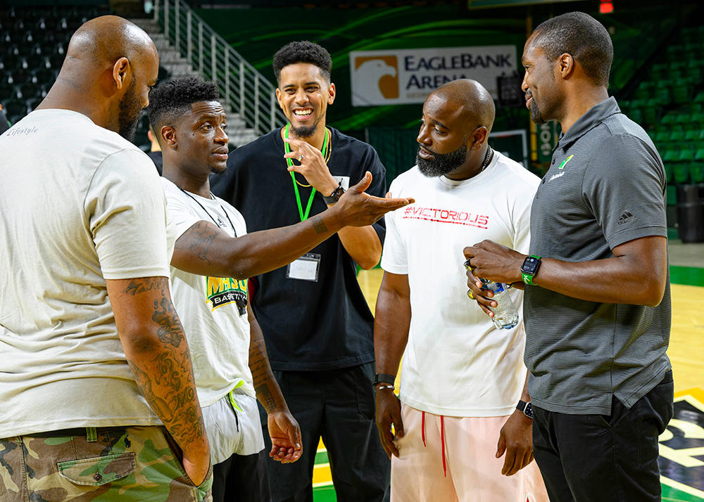 Five men are having a conversation in the middle of a basketball court.