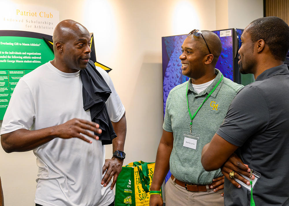 Three people in Mason Athletics attire stand chatting.