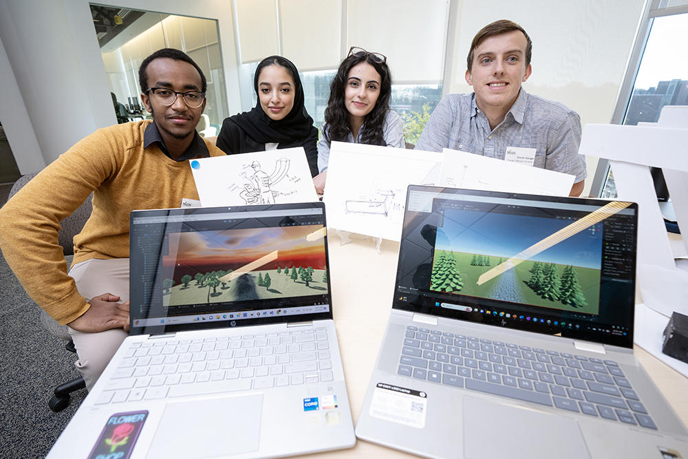 Students sit behind two laptops and sketches showcasing their work