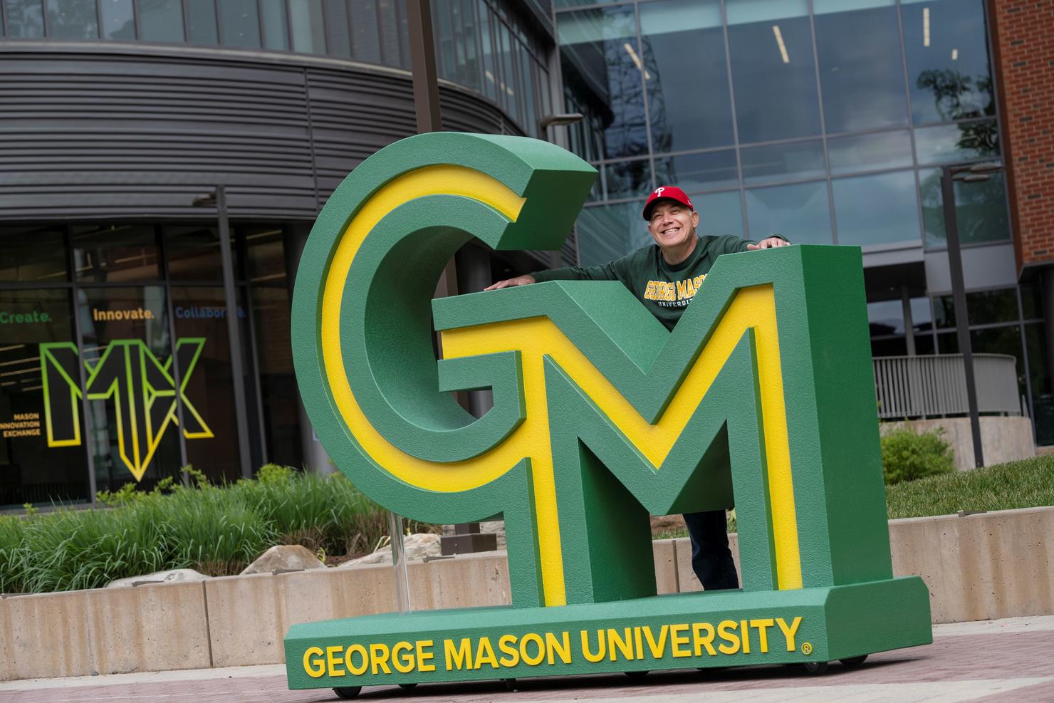 George Mason staff member stands with the new logo installation on campus