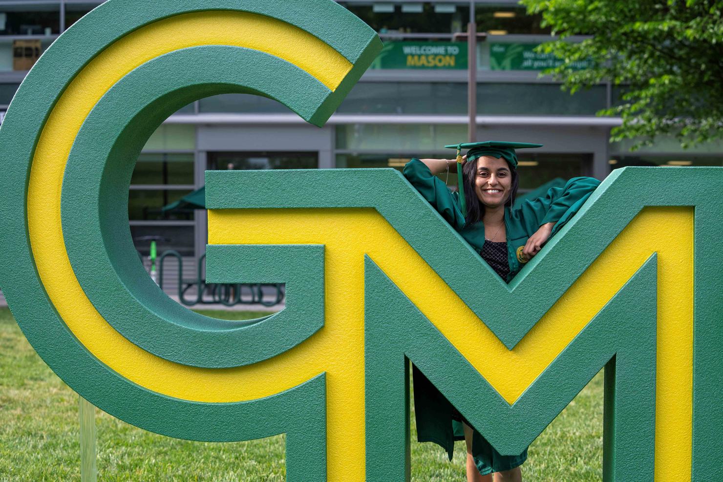 Graduate in regalia poses with George Mason logo installation
