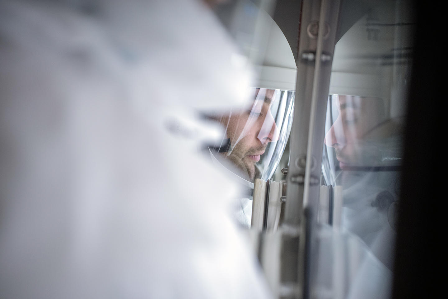 Researcher in a biohazard suit looks through a protective window in a lab