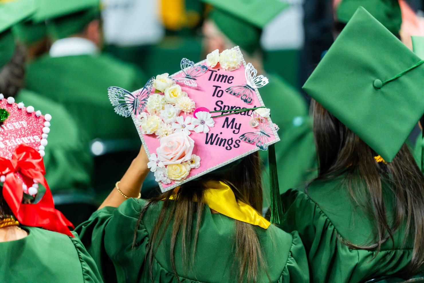 A graduate wears a decorated cap with faux butterflies and the words "time to spread my wings"