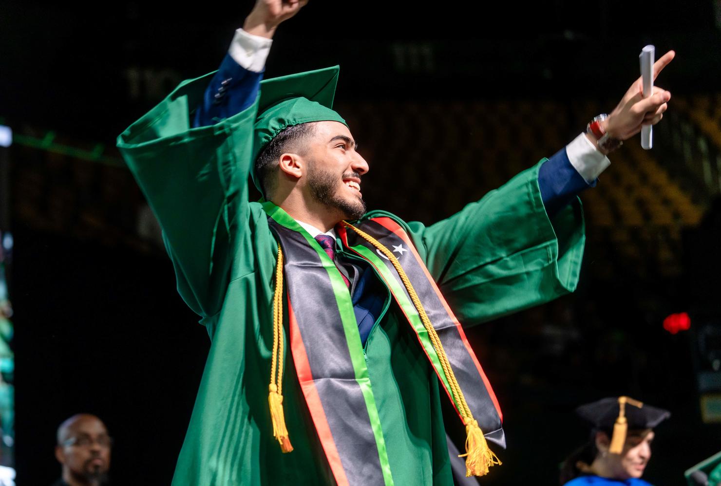 A graduating student raises his hands in the air and points at his family and friends in the crowd