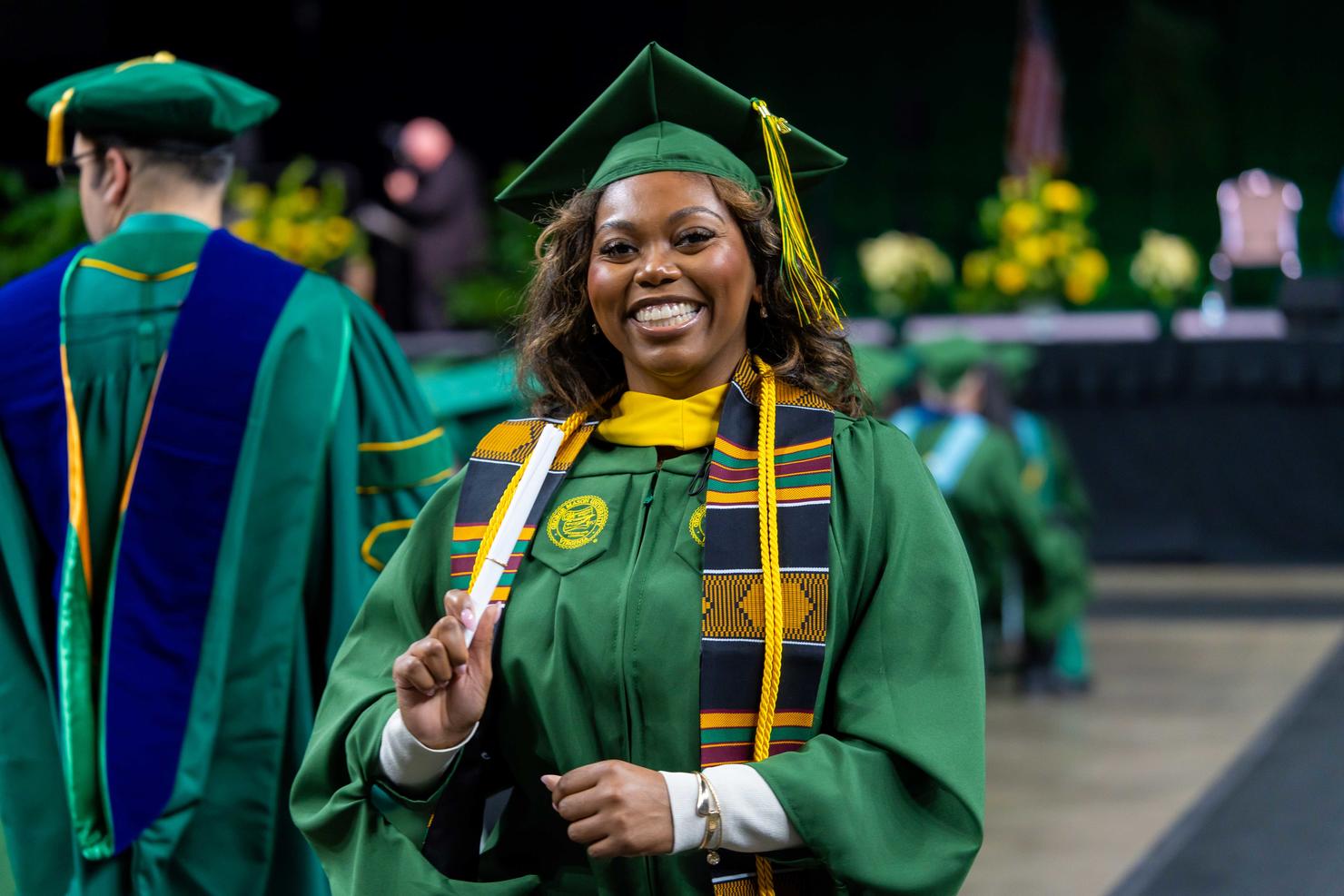 Graduate smiles holding her scroll after walking across the stage