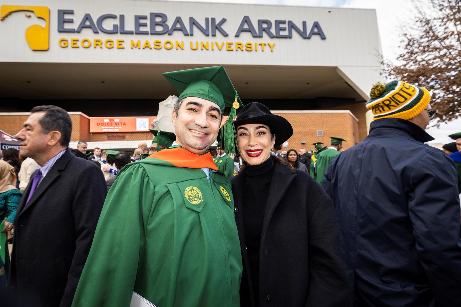 A graduate in regalia smiles with a loved one outside EagleBank Arena
