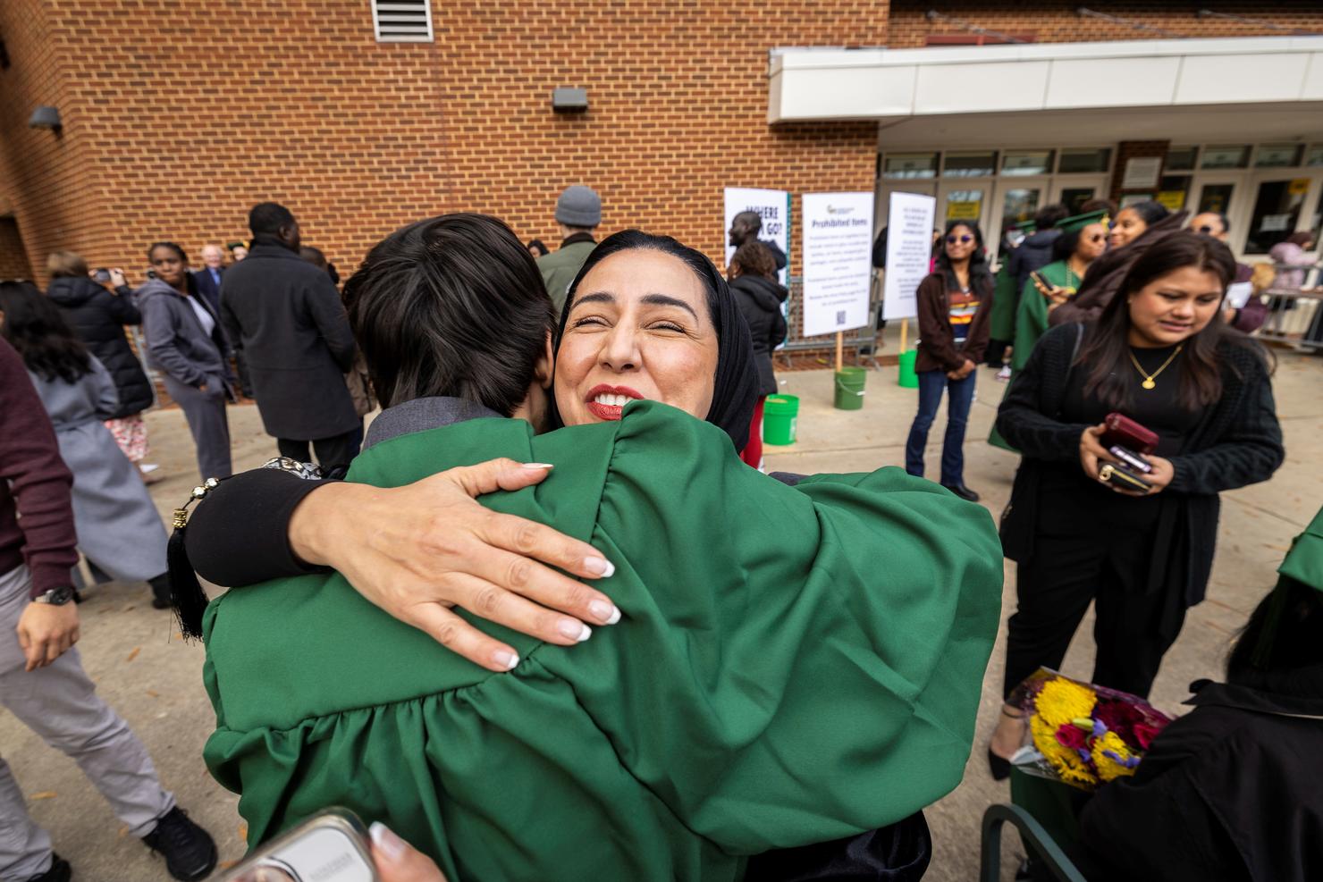 A graduate smiles while embracing a loved one outside the arena after Commencement