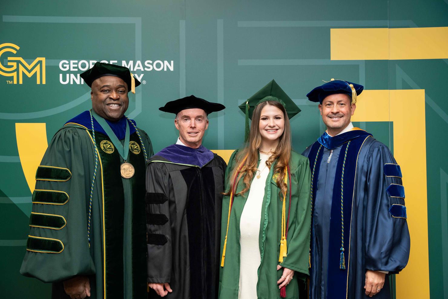 President Gregory Washington, Rector Charles "Cully" Stimson, Student Speaker Caroline Little, and Provost James Antony gather for a photo in front of a George Mason branded backdrop