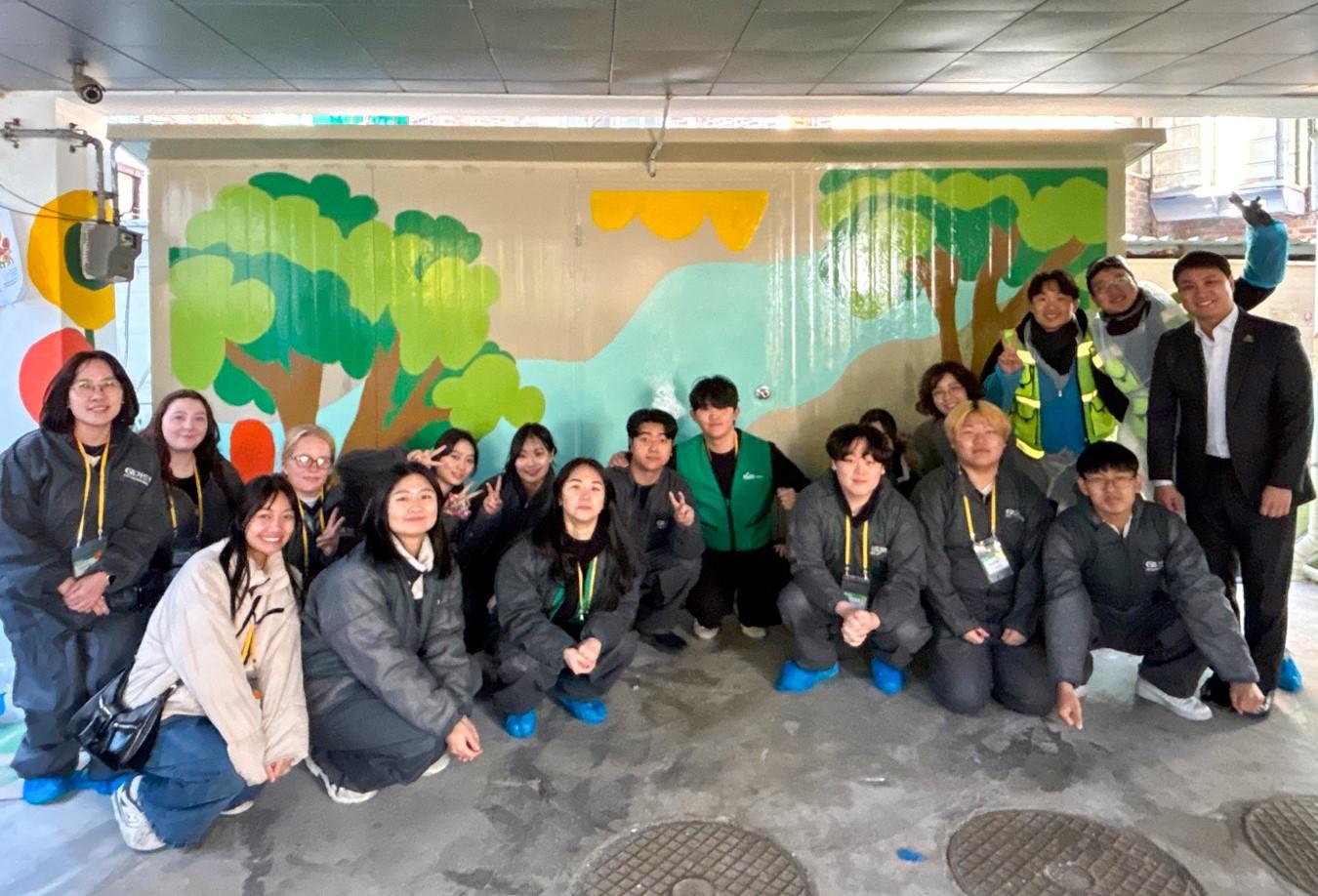 Volunteers gather for a group photo in front of a mural of an outdoor scene