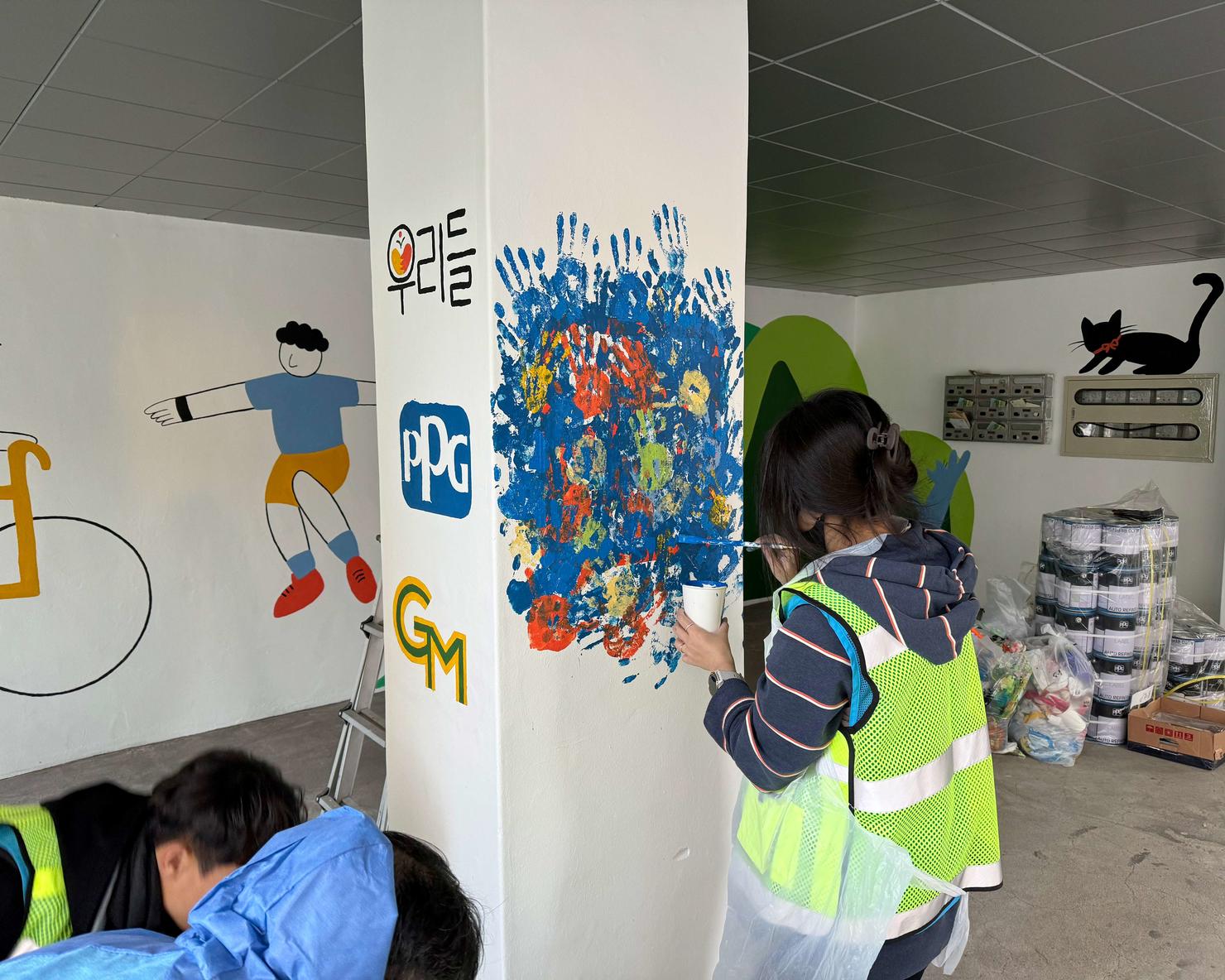 A volunteer paints bright colors onto a pillar at the youth home, featuring a George Mason University logo