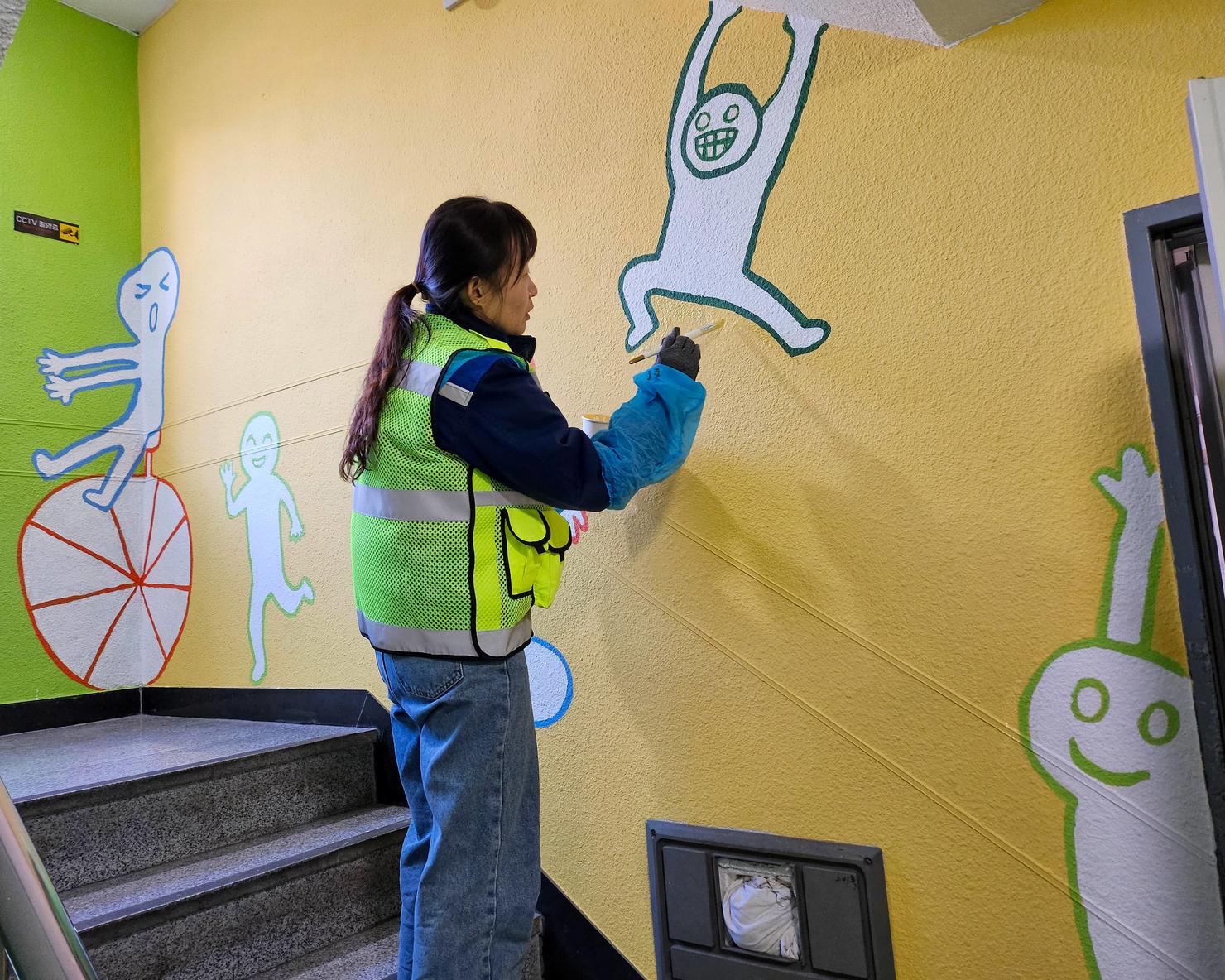 Volunteer paints the wall of a stairwell with a bright design featuring cartoon human figures