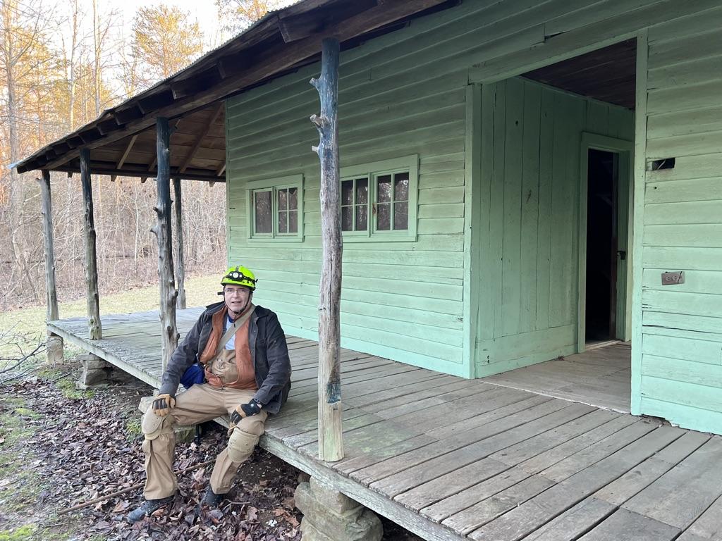 Buz Grover wears his cave-exploring gear while sitting on the front porch of a cabin