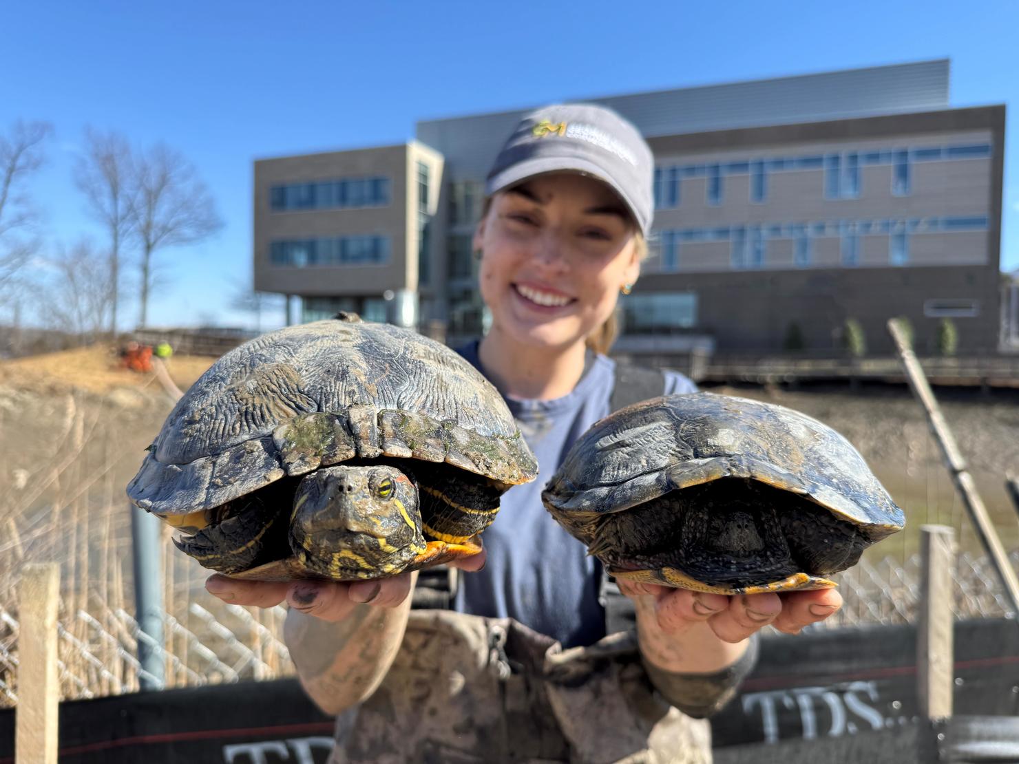 Student Rylee Ledoux holds two rescued turtles in her hands, with the Potomac Science Center in the background