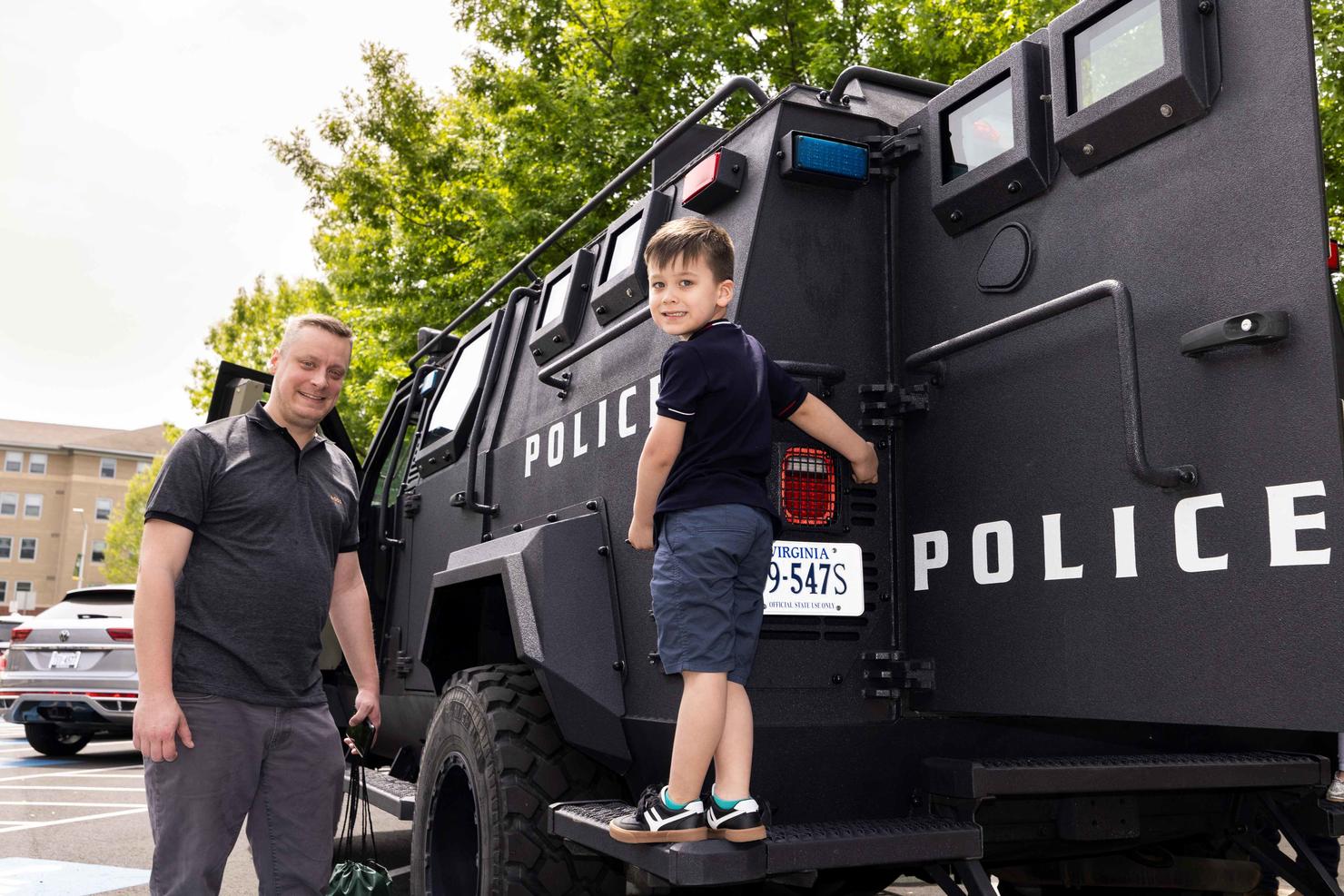 A child climbs on a large police vehicle with his father nearby at the touch-a-truck event