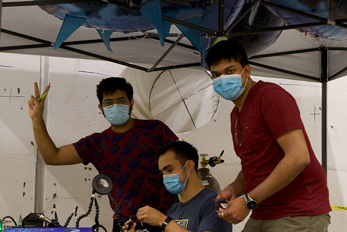 Three teammates wearing masks pose for a photo under a tent.
