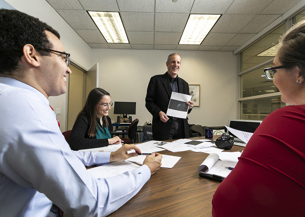 Innovation Law Clinic. Three law students sit around the table while an instructor discuss intellectual property law.