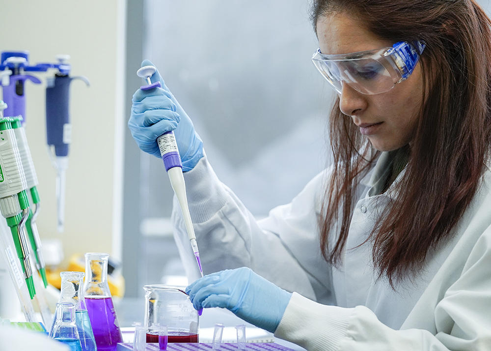 Student in white lab coat and blue lab gloves works in the neurscience lab