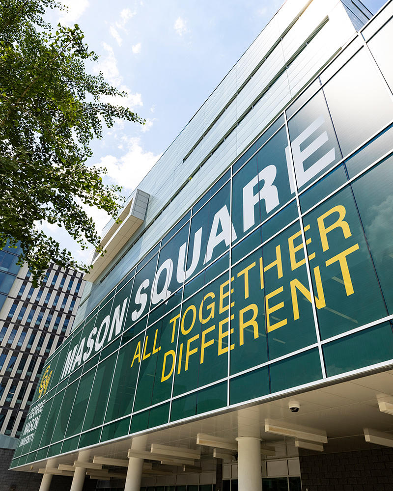 exterior of Van Metre hall, focussed on the window clings that read: George Mason University, Mason Square, All Together Different