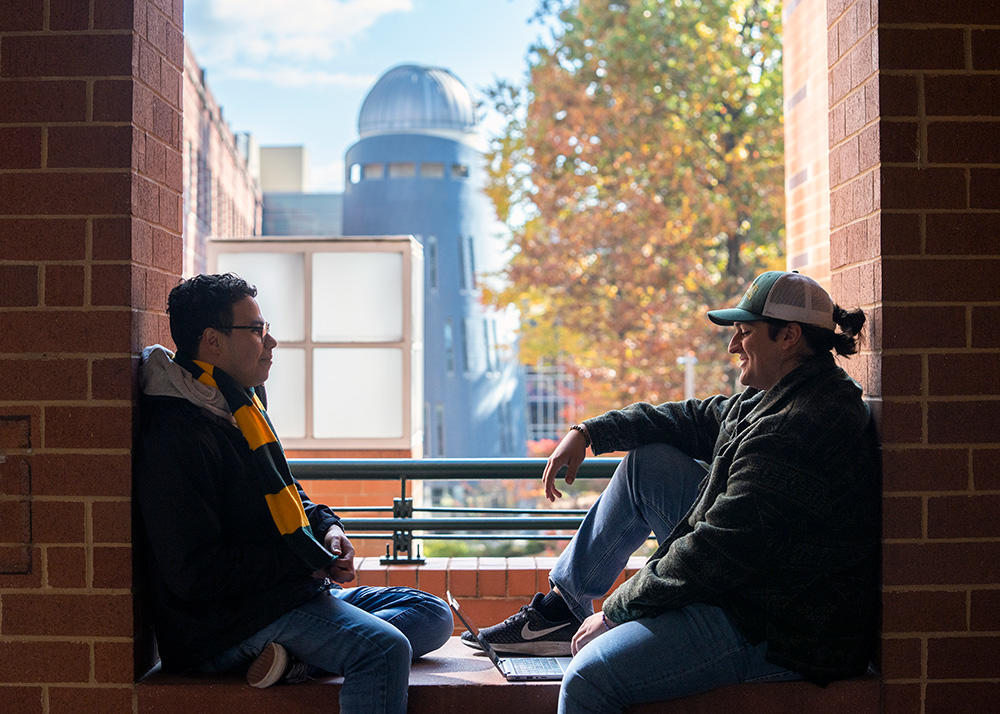 Two students sit on a brick wall. In the background, one can see the campus telescope atop a tower.