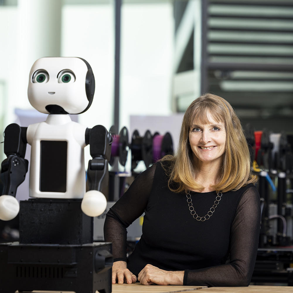 Missy Cummings headshot. Missy poses next to a robot.