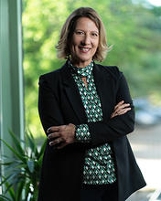 Melissa Perry stands next to a window an wears a black blazer and green print blouse