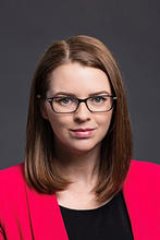 Evan Lowder is wearing a bright pink blazer and black top and wears glasses