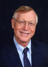 R Christian Jones wears a blue sportcoat, light blue button-up shirt and blue tie