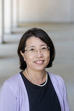 Xiaomei Cai is wearing a dark top, light cardigan sweater and pearls