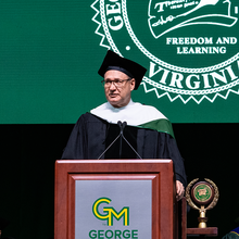 Shindler speaking at a George Mason University branded podium