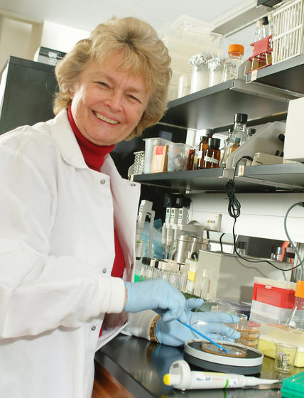 Jenefir Isbister smiles at the camera wearing a lab coat in her lab.