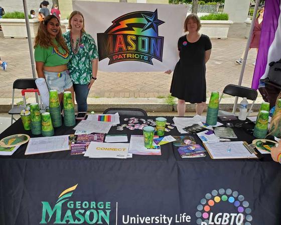 Members and supporters of the LGBTQ+ Resource center staff the center's table at Mason's welcome week. The table is stocked with various pride buttons, pride t-shirts, resource guides and other goodies.
