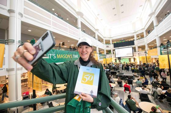 A female student takes a selfie in the Johnson Center atrium at Mason's 50th anniversary celebration