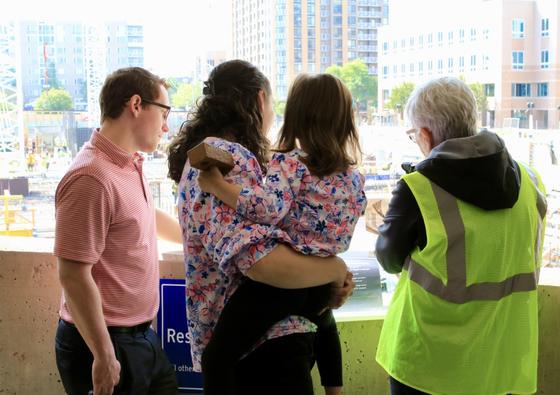Three adults and one child look down at the construction site of Fuse at Mason Square from a nearby parking garage.