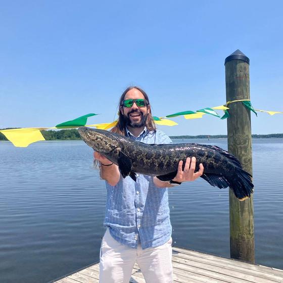 Reid Nelson holds a snakehead, an invasive species of fish, on the dock at the Potomac Science Center