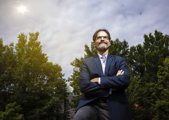 Peter Becker stands outside in the sunlight before a group of trees, his eyes towards the sky.